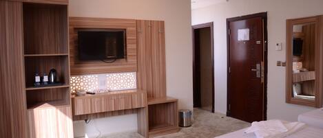 Habitación de hotel con un armario de madera, un televisor montado en la pared, un escritorio pequeño con una lámpara y dos camas con toallas.
