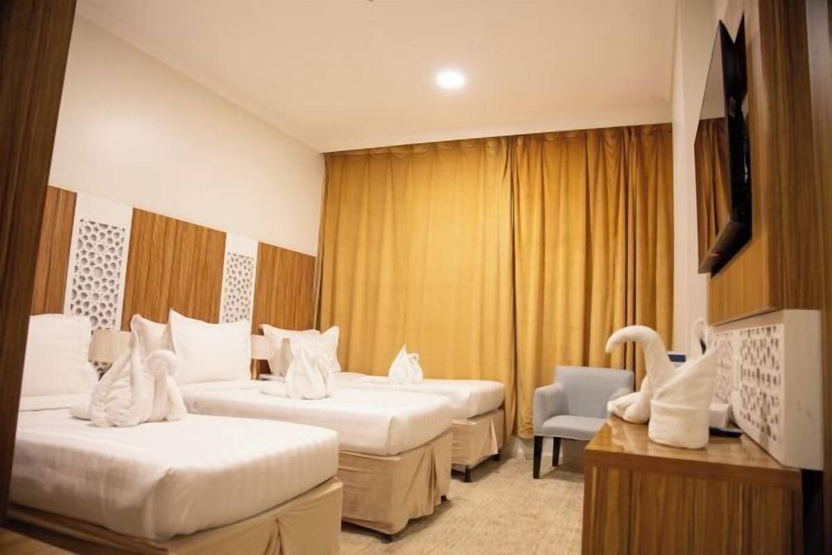 A hotel room with two beds, a desk, a chair, and a large window with curtains.