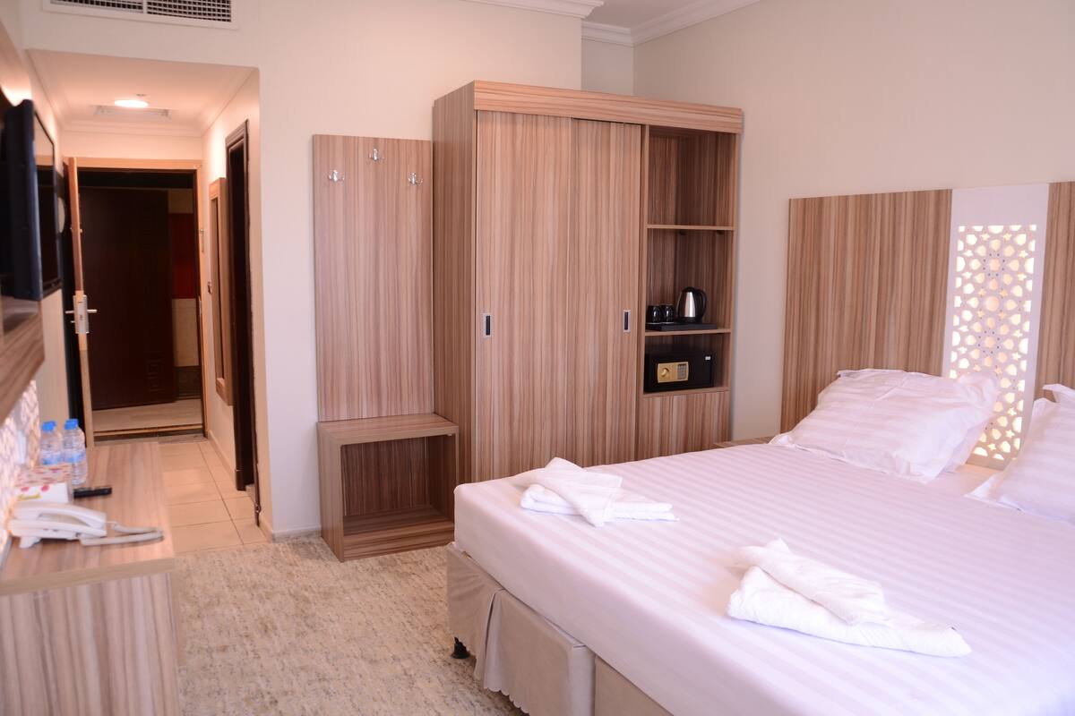 A hotel room with a large bed, a wardrobe, a desk with a telephone, and a bathroom visible through an open door.