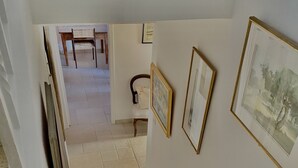 A staircase with beige tiles leading to a room with white walls. There are framed pictures on the walls and a wooden chair in the room. - Charming, bright house 10 minutes from the village center (Collioure)