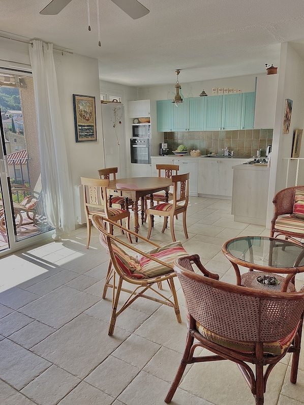 A spacious living area with a dining set, wicker chairs, and a glass-top coffee table.
