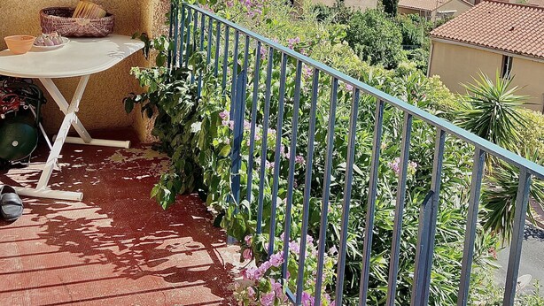 A balcony with a table and chairs, a decorative wall piece, and a view of a hillside town. - Charming, bright house 10 minutes from the village center (Collioure)