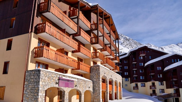 Un hotel de varios pisos con balcones de madera y arquitectura de piedra, con una imponente montaña nevada de fondo.