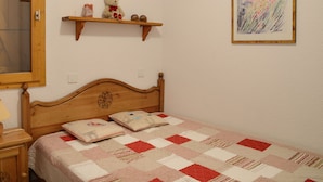 Un dormitorio con una cama de madera, un edredón, una estantería con un osito de peluche y un cuadro enmarcado.