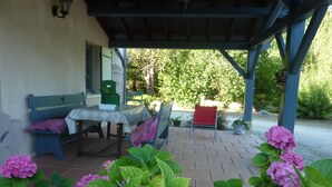 Une terrasse extérieure avec une table et des chaises, un banc et des plantes en pot.