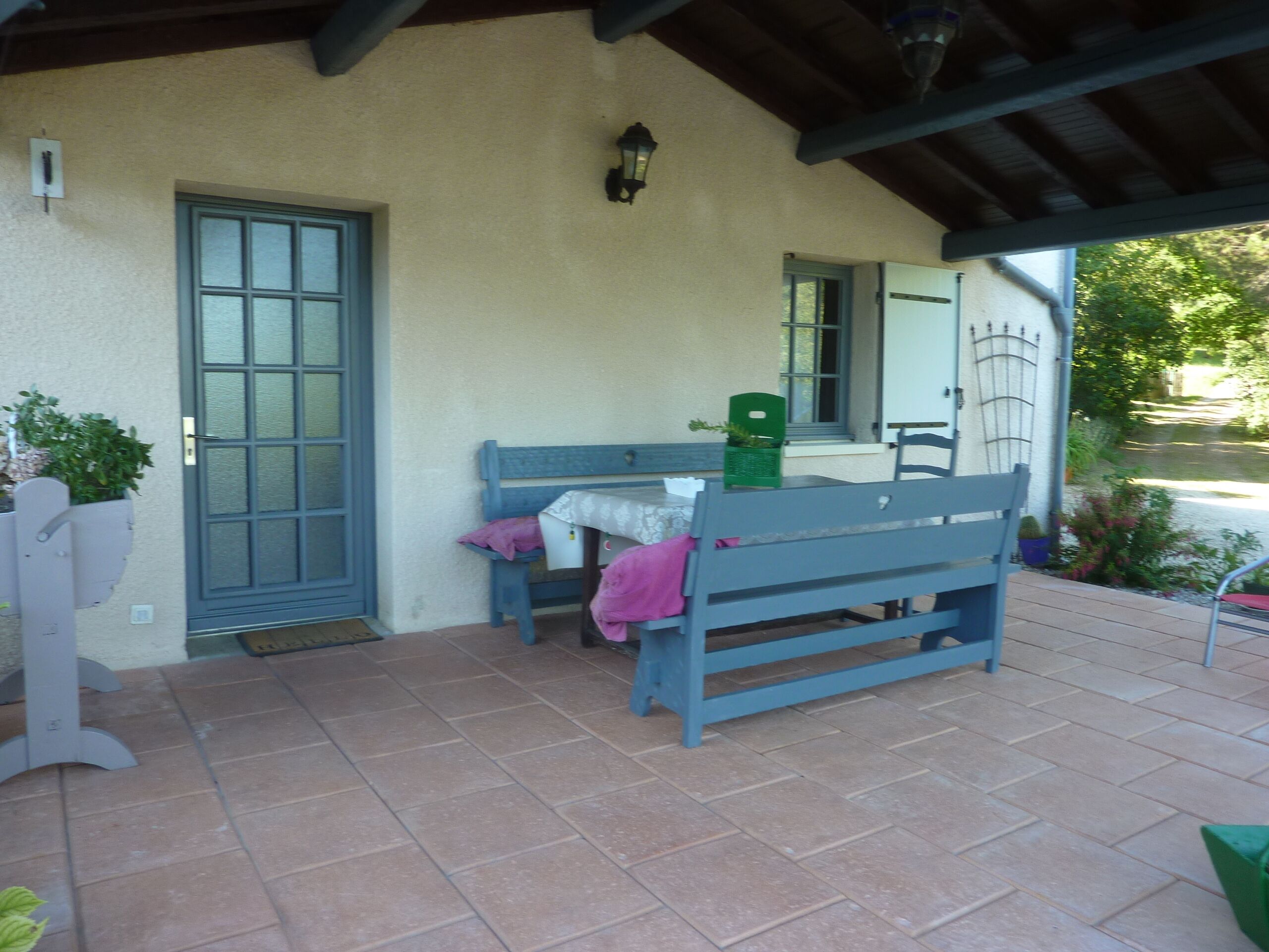 Un patio abrité avec une table et des bancs, une porte et un petit jardin.