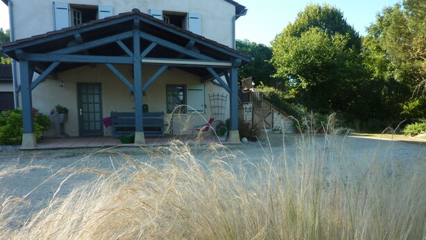 Un bâtiment doté d’un porche couvert, d’un banc et d’une allée gravillonnée.