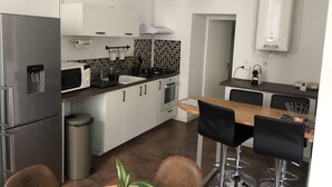 A modern kitchen with white cabinets, a stainless steel refrigerator, a microwave, and a sink. There is a dining area with a wooden table and black chairs. - ?appartement Futuroscope T2 ? Cosyhousebyjanna? (POITIERS)