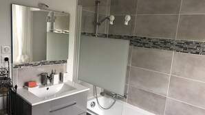 A modern bathroom with a large mirror, a white sink, a shower with a handheld showerhead, and grey tiled walls. - ?appartement Futuroscope T2 ? Cosyhousebyjanna? (POITIERS)