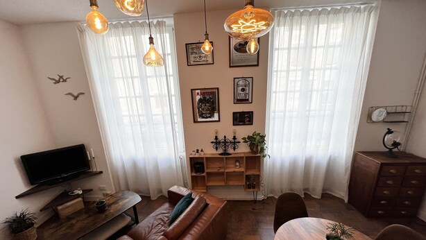 A living room with a brown leather sofa, a wooden dining table with chairs, a TV on a stand, and pendant lights. - ?appartement Futuroscope T2 ? Cosyhousebyjanna? (POITIERS)