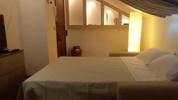 A hotel room with a bed, a television, and a vase on a nightstand. - Attic apartment iPatrizi (Moncalieri)