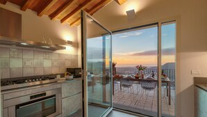 Une cuisine moderne dotée d’un grand îlot central, d’un coin repas offrant une vue agréable et d’une porte-fenêtre coulissante donnant sur une terrasse extérieure.