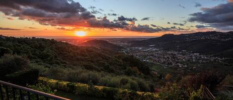 Vista panoramica di una città al tramonto, con in primo piano dolci colline verdi e una ringhiera.