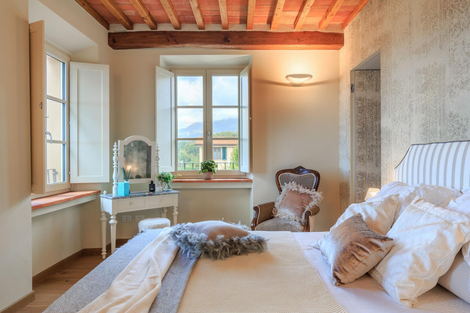 A bedroom with a bed, a chair, a desk, and a window with a view of the mountains.