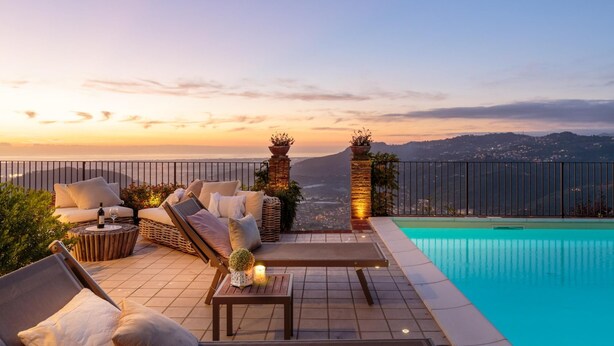 Une terrasse sur le toit avec une piscine, des chaises longues et une vue sur la ville au coucher du soleil.
