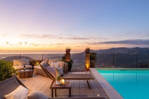 Eine Dachterrasse mit Pool, Liegestühlen und Blick auf die Stadt bei Sonnenuntergang.