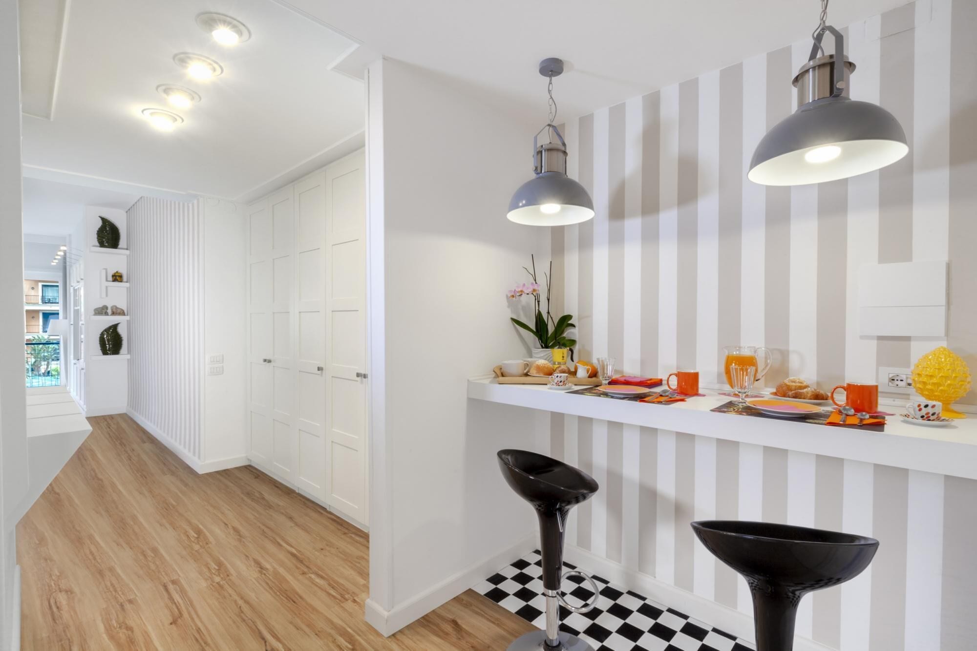 Una cocina moderna con armarios blancos, piso a cuadros y una zona para desayunos con tazas naranjas y un frutero.