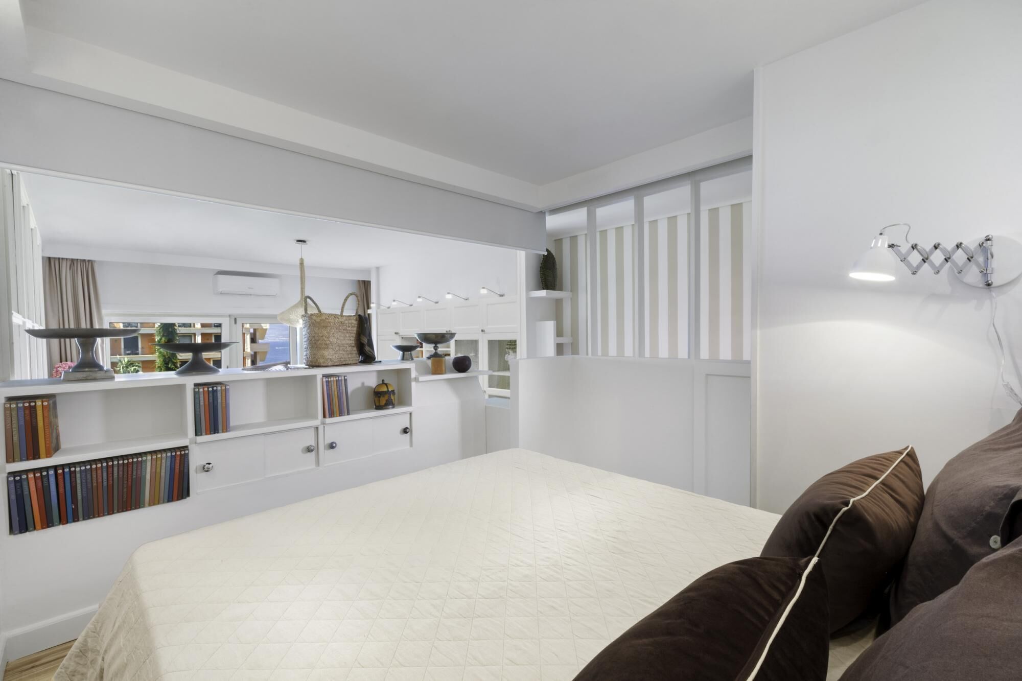 A modern bedroom with a large bed, built-in bookshelves, a bedside table, and a hanging lamp.