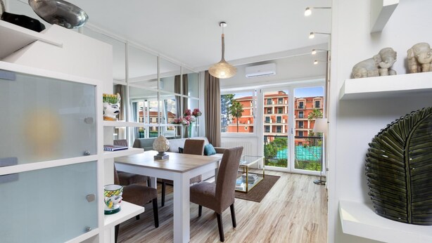 A modern dining area with a wooden table, chairs, and a view of a red building through large windows. - Bed and Breakfast Sorrento 7 Flat (Sorrento)