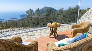 A terrace with wicker furniture, a small table with a fruit bowl, and a view of the sea and mountains. - Villa Ligea in Sant Agata sui Due Golfi (Massa Lubrense)