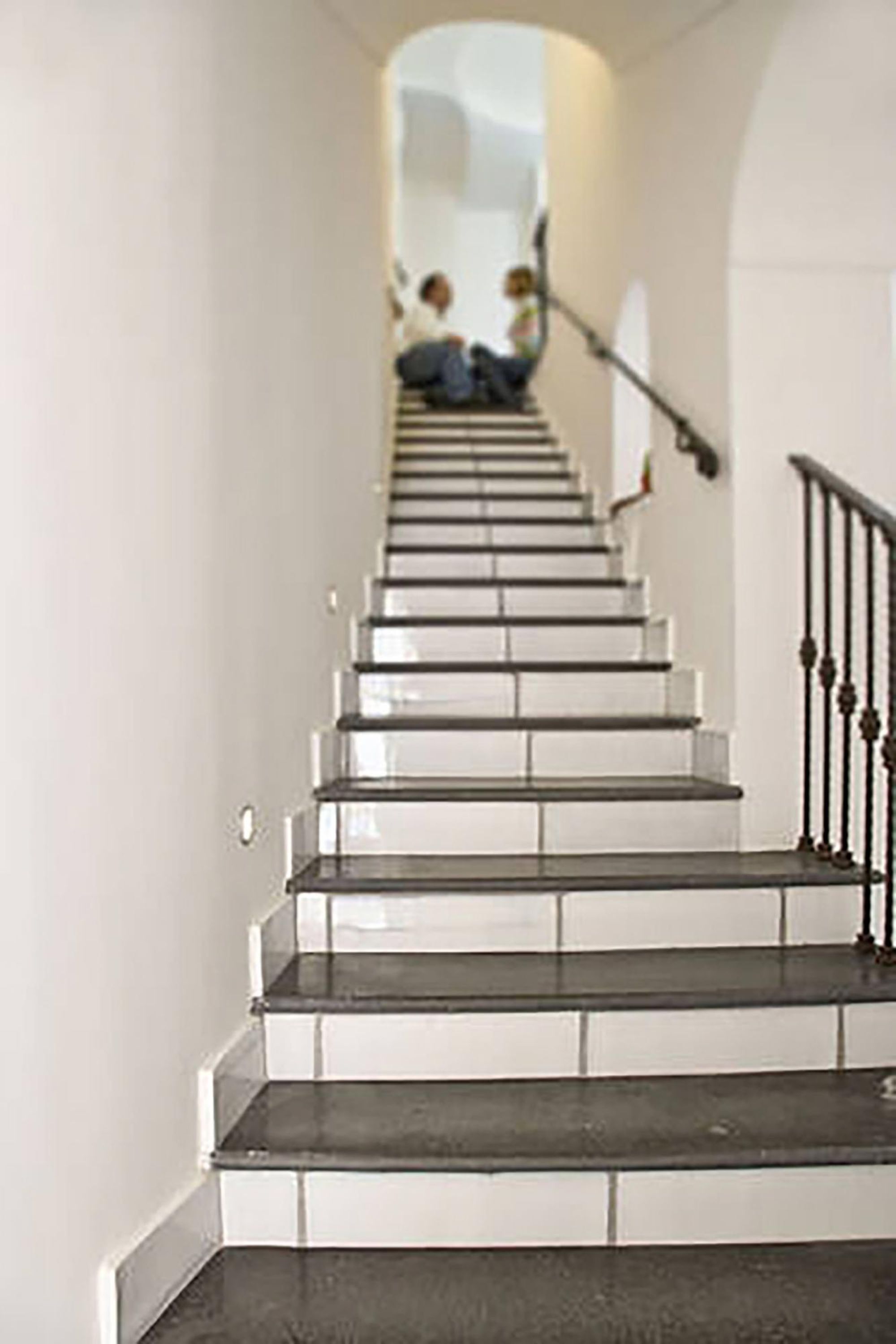 Eine Treppe mit weißen Stufen und einem schwarzen Geländer, die zu einer Aussichtsplattform führt, wo Menschen sitzen.