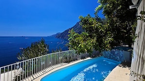 A swimming pool with a curved edge, surrounded by a white metal fence and lush greenery. - Villa Le Sirene in Positano (Positano)