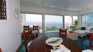 A spacious room with a large dining table, a sofa, and a view of the ocean. - Villa Le Sirene in Positano (Positano)