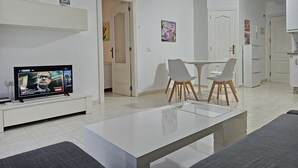 A modern living room with a flat-screen TV, a glass-top coffee table, and a dining area with two chairs. - TIJERITAS COOL SEA BREEZE (Los Cristianos)