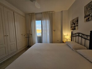 A bedroom with a large bed, a wardrobe, a window with curtains, and a painting on the wall.