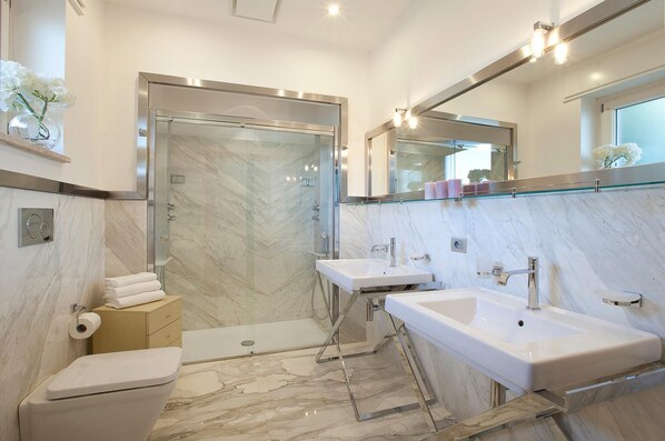 A modern bathroom with a toilet, shower, and two sinks.