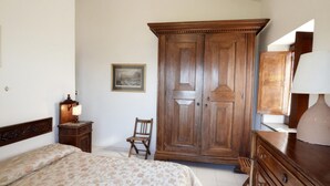 A bedroom with a bed, a wooden wardrobe, a chair, a nightstand with a lamp, and a dresser. - Villa Posidonia in Massa Lubrense (Massa Lubrense)