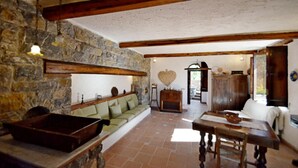 A rustic interior with a stone wall, wooden beams, a green sofa, a wooden table, and a tiled floor. - Villa Posidonia in Massa Lubrense (Massa Lubrense)