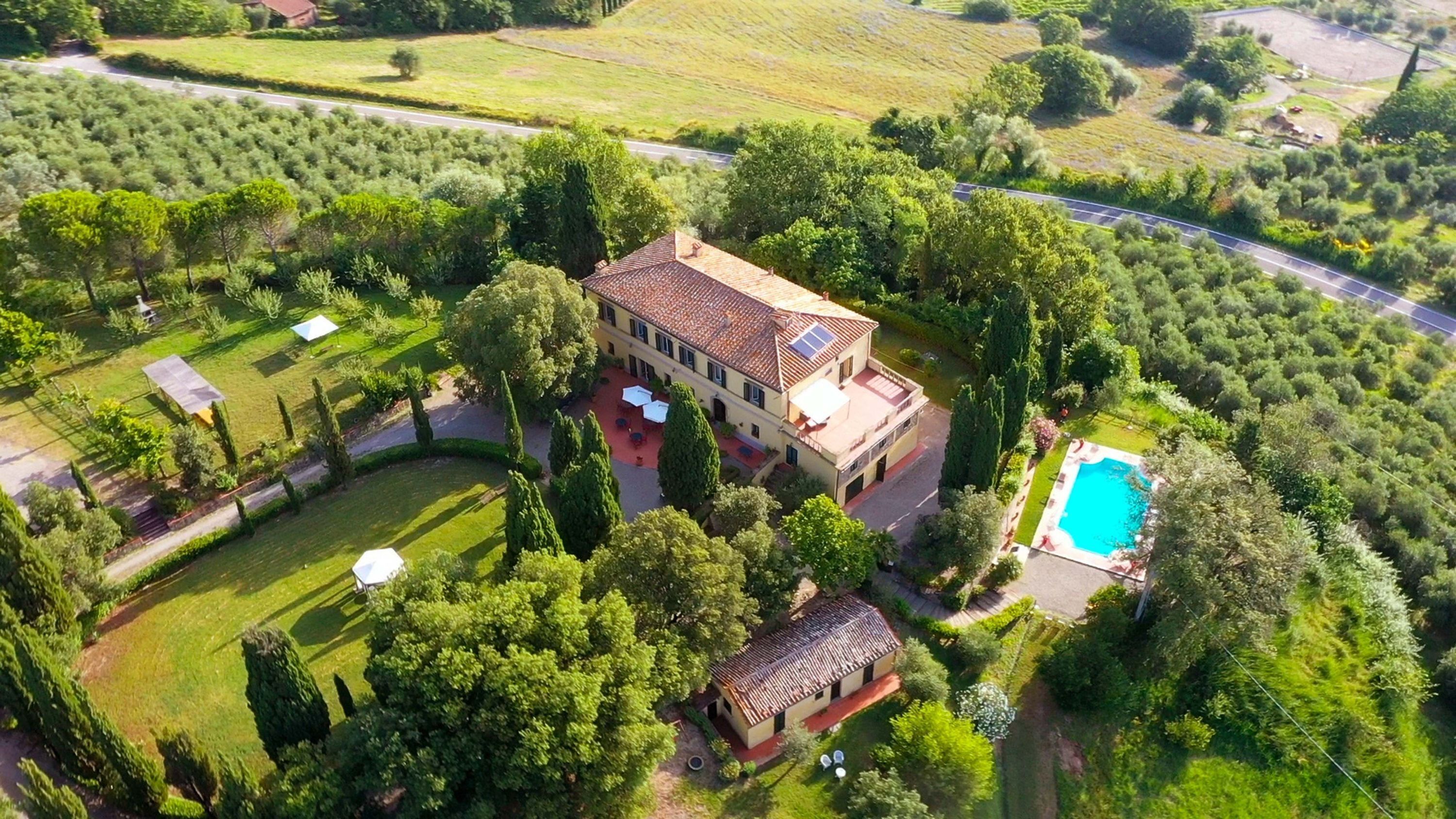 A large house with a swimming pool, surrounded by lush greenery and a well-maintained lawn.