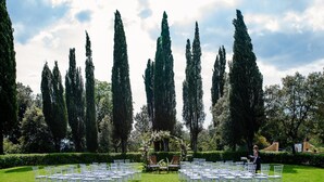 A formal outdoor seating area with rows of white chairs, a central floral arrangement, and tall cypress trees in the background. - Villa Il Giardino in Radicofani (Radicofani)