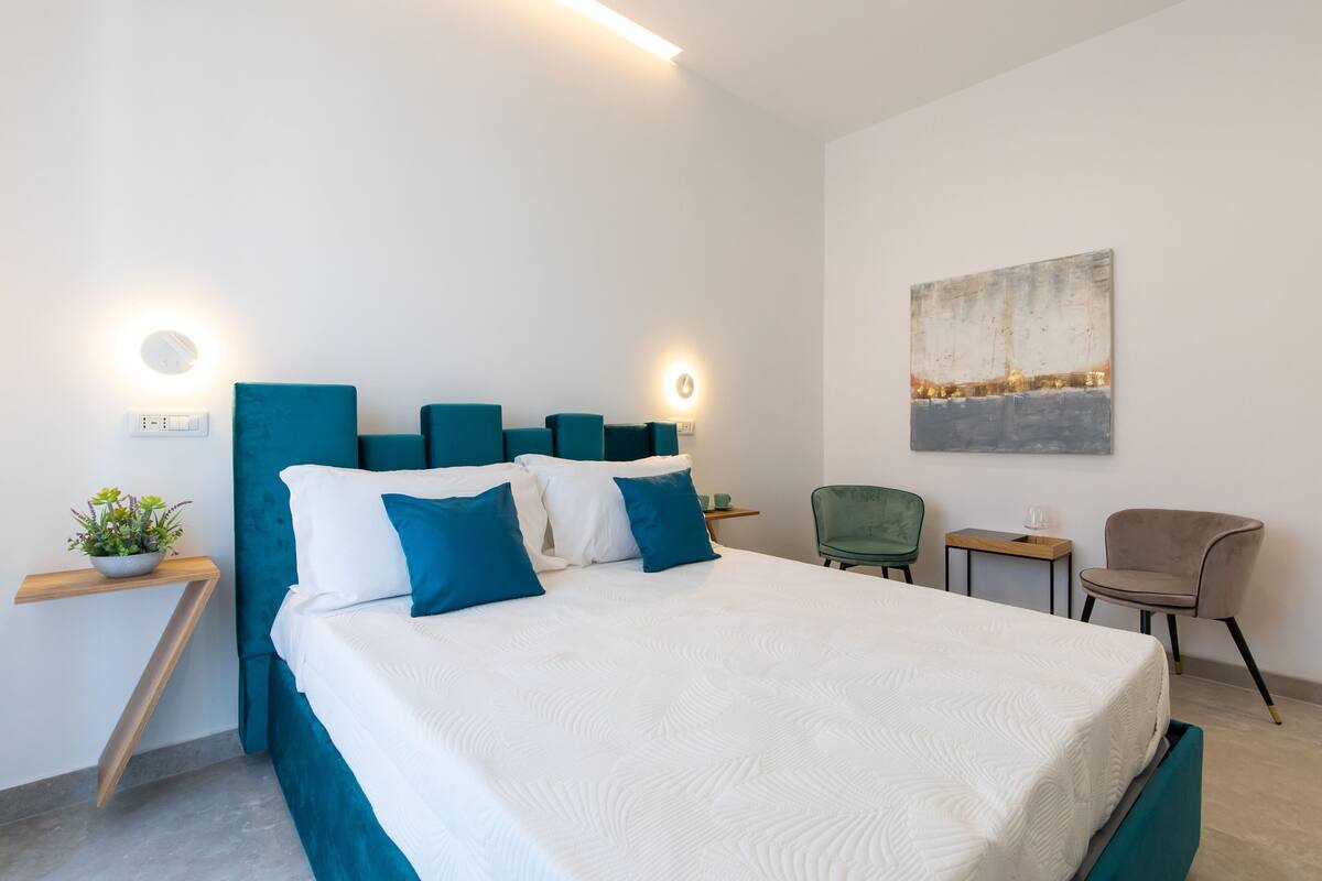 A modern bedroom with a bed, bedside tables, a small plant, and a painting on the wall.
