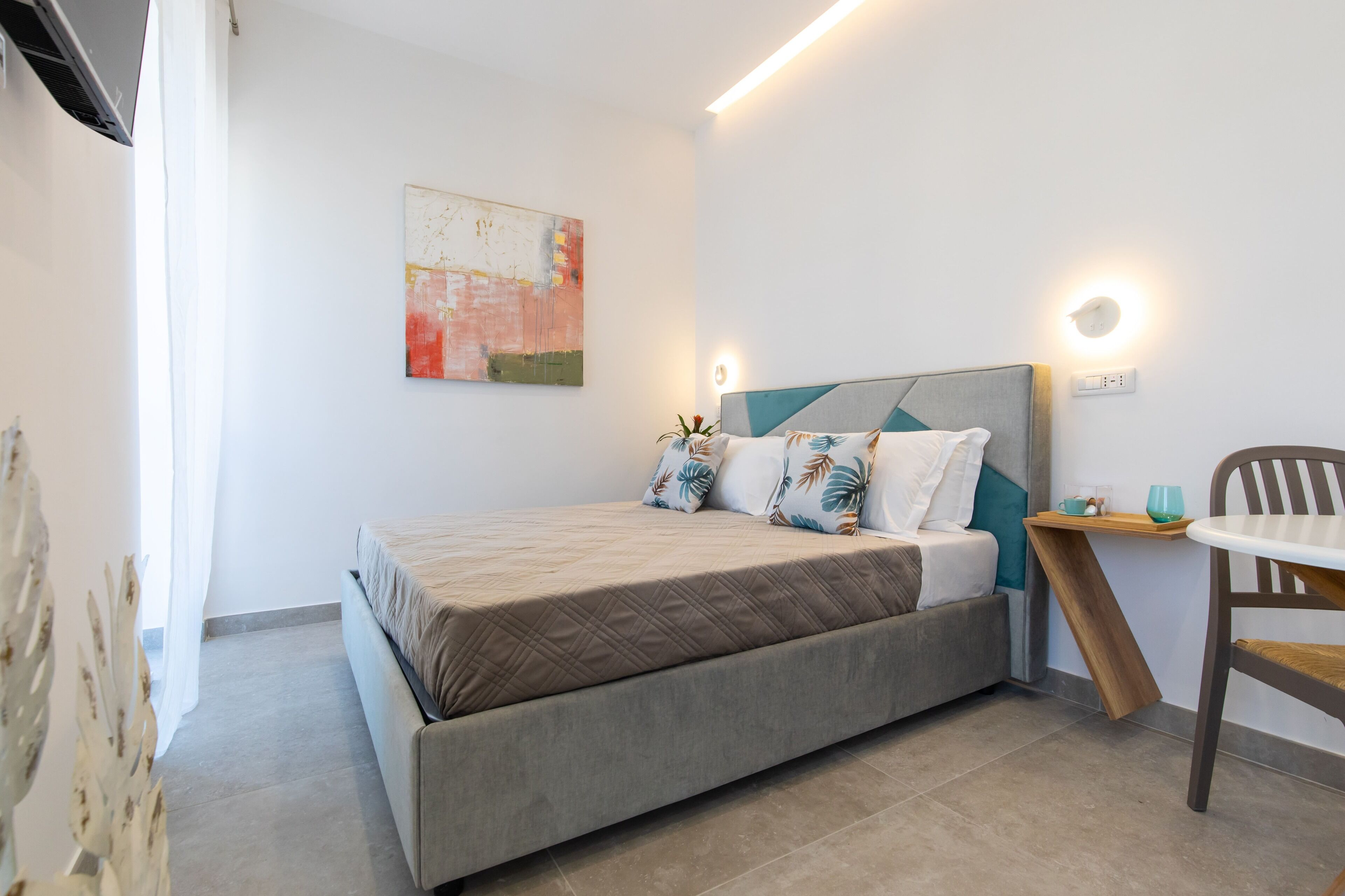 Une chambre à coucher comprenant un lit, une table de chevet avec une lampe, une chaise et une œuvre d’art accrochée au mur.