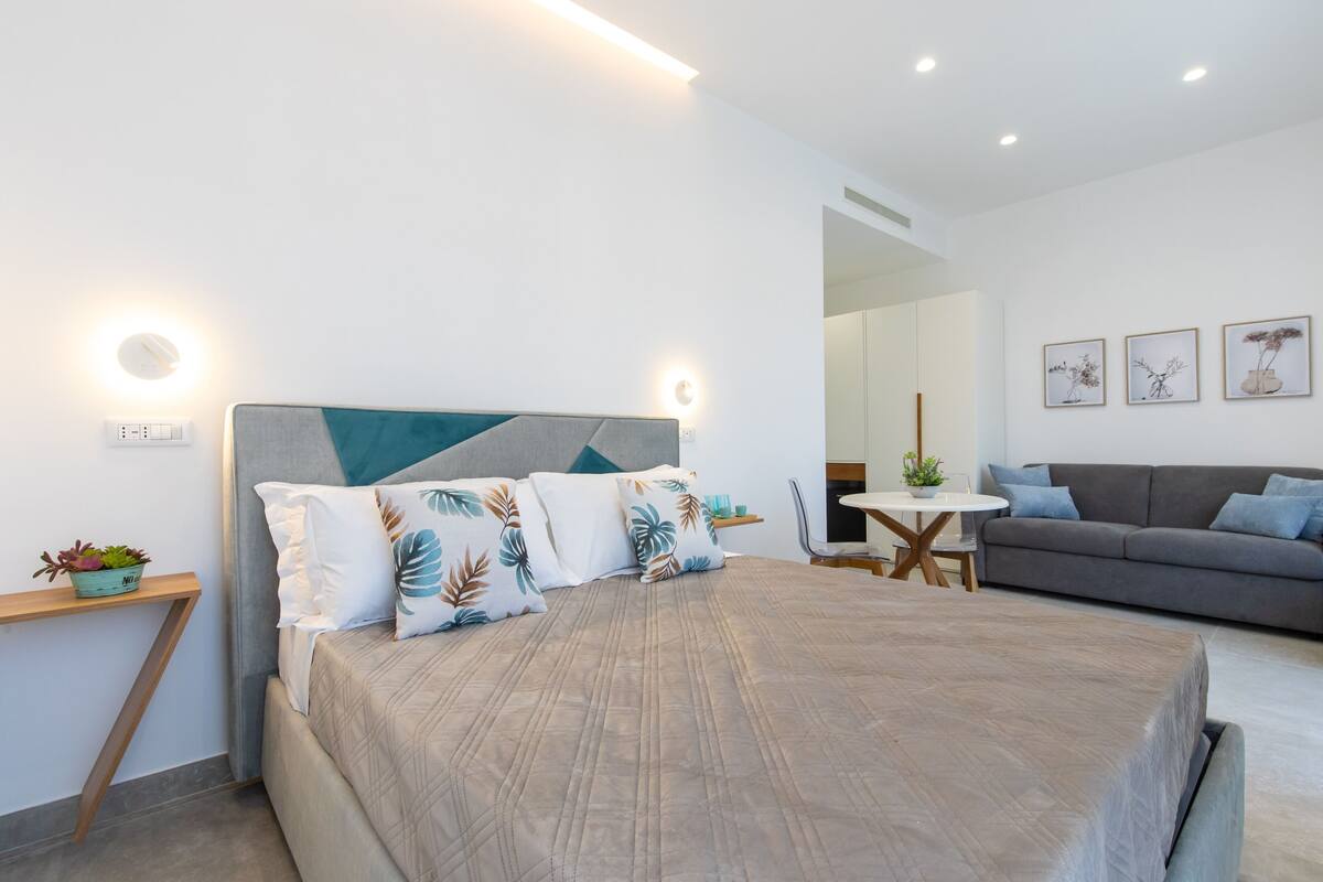 A modern bedroom with a bed, bedside table, and a sofa.