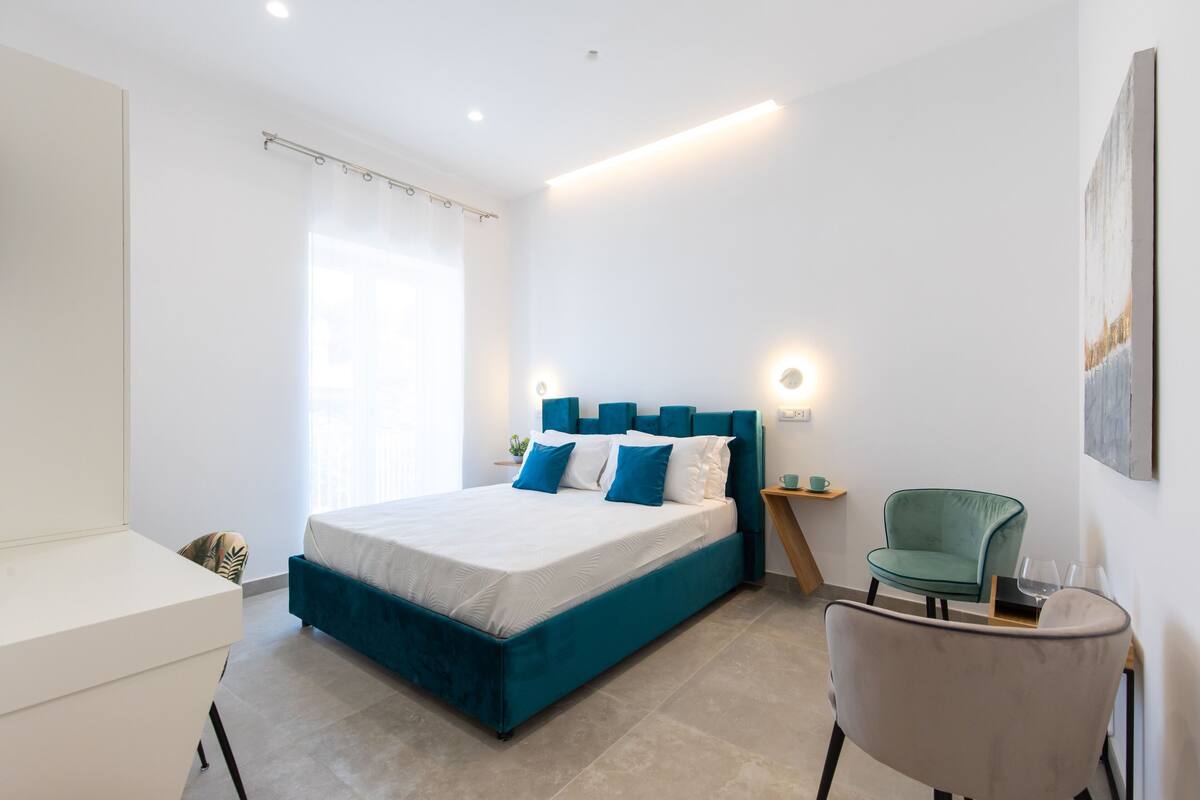 A modern bedroom with a large bed, a green chair, and a bedside table with a lamp.