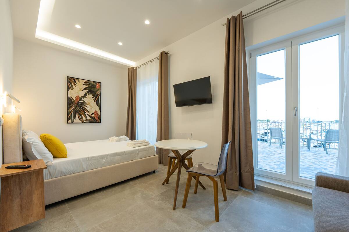 A modern hotel room with a bed, a small table, a TV, and a view of the outside.