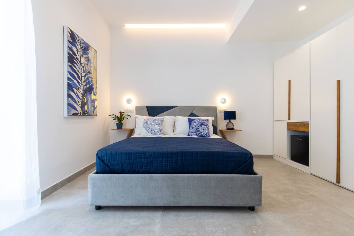 A modern bedroom with a bed, bedside tables, a nightstand, a potted plant, and a wardrobe.