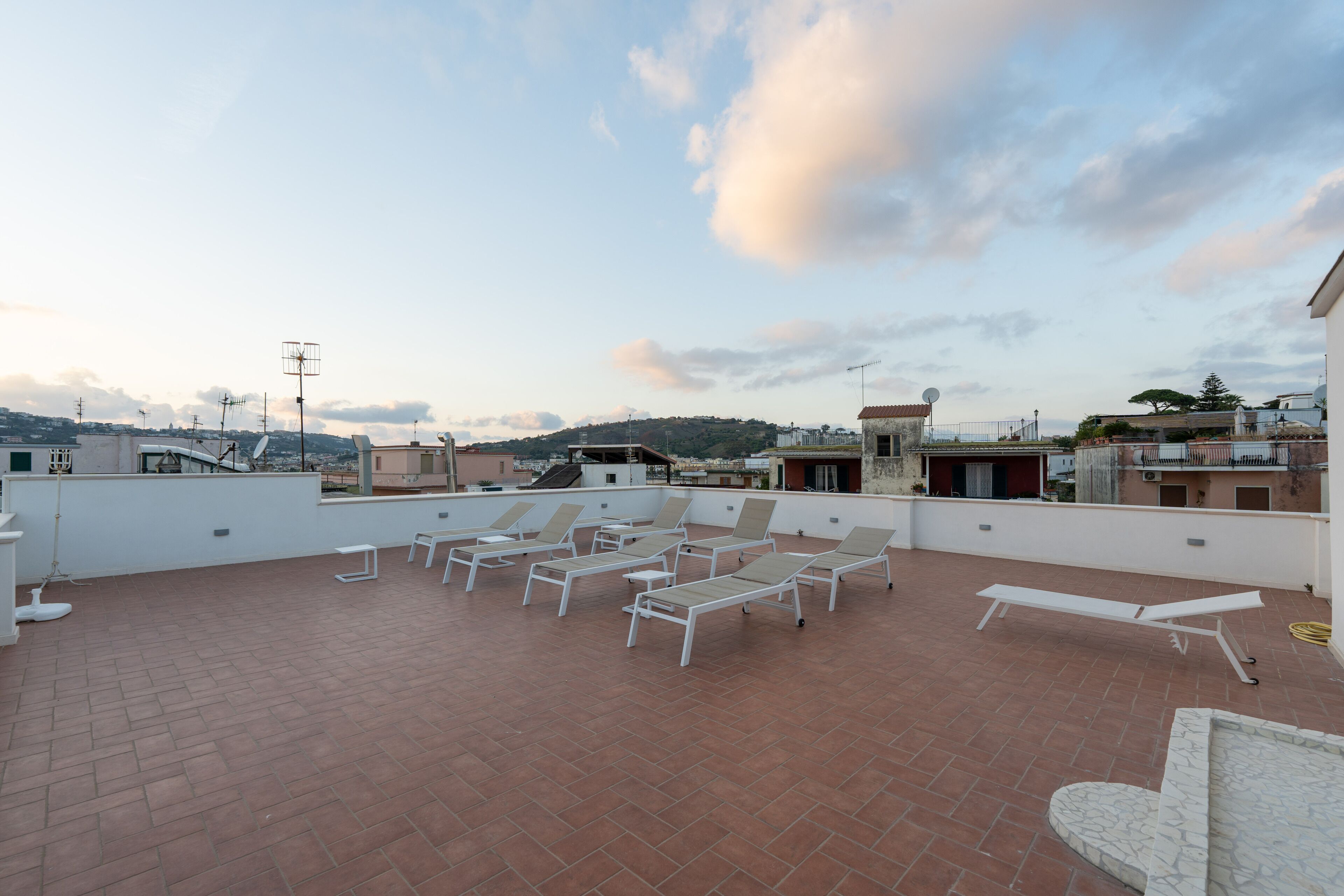 A rooftop terrace with several sun loungers and a white wall.