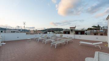 A rooftop terrace with several sun loungers and a white wall.