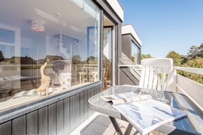 Un balcone con un tavolo in vetro, sedie e una porta vetrata che dà sull'interno.