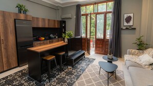 Eine moderne Küche mit eingebautem Kühlschrank, Holzschränken und einer Bar. Ein großes Fenster mit Vorhängen, eine Sitzecke mit einer Couch und einem Couchtisch sowie ein gemustertes Teppich sorgen für Gemütlichkeit.