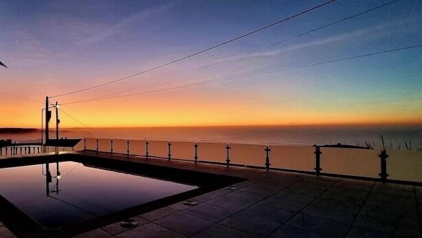 A sunset view from a balcony with a pool and a railing overlooking the sea. - Mae Home-Galaxy (Foz do Arelho)