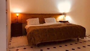 A bedroom with a wooden headboard, two bedside lamps, a bed with a patterned bedspread, and a white rug. - Mae Home-Galaxy (Foz do Arelho)