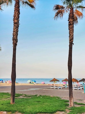 Ein Strand mit Palmen, Strandliegen und Sonnenschirmen.