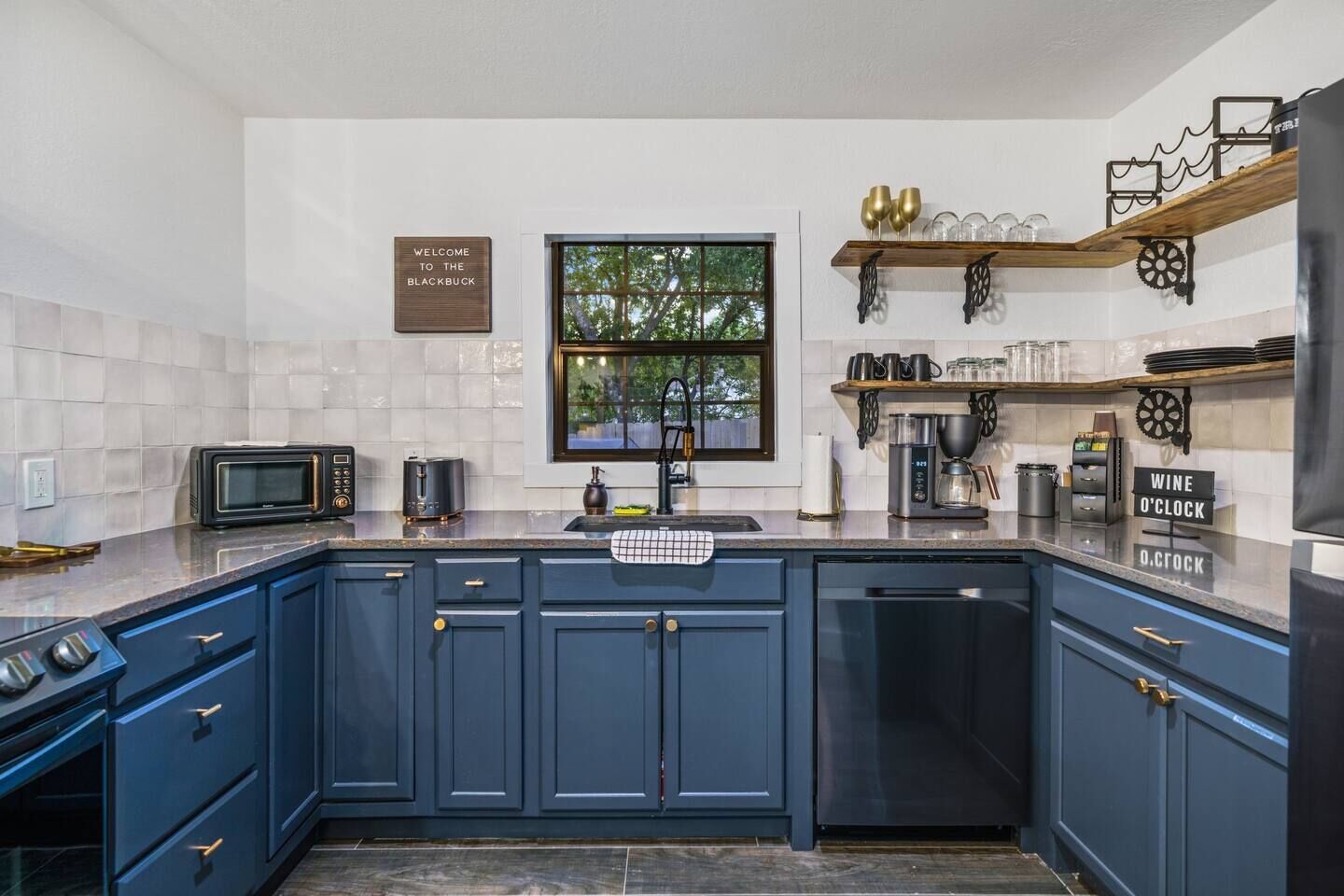 A modern kitchen with dark blue cabinets, a built-in oven, a microwave, a coffee maker, and a wine o'clock sign.