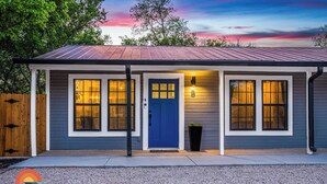 A single-story house with a blue front door, two large windows on either side, and a small porch area.