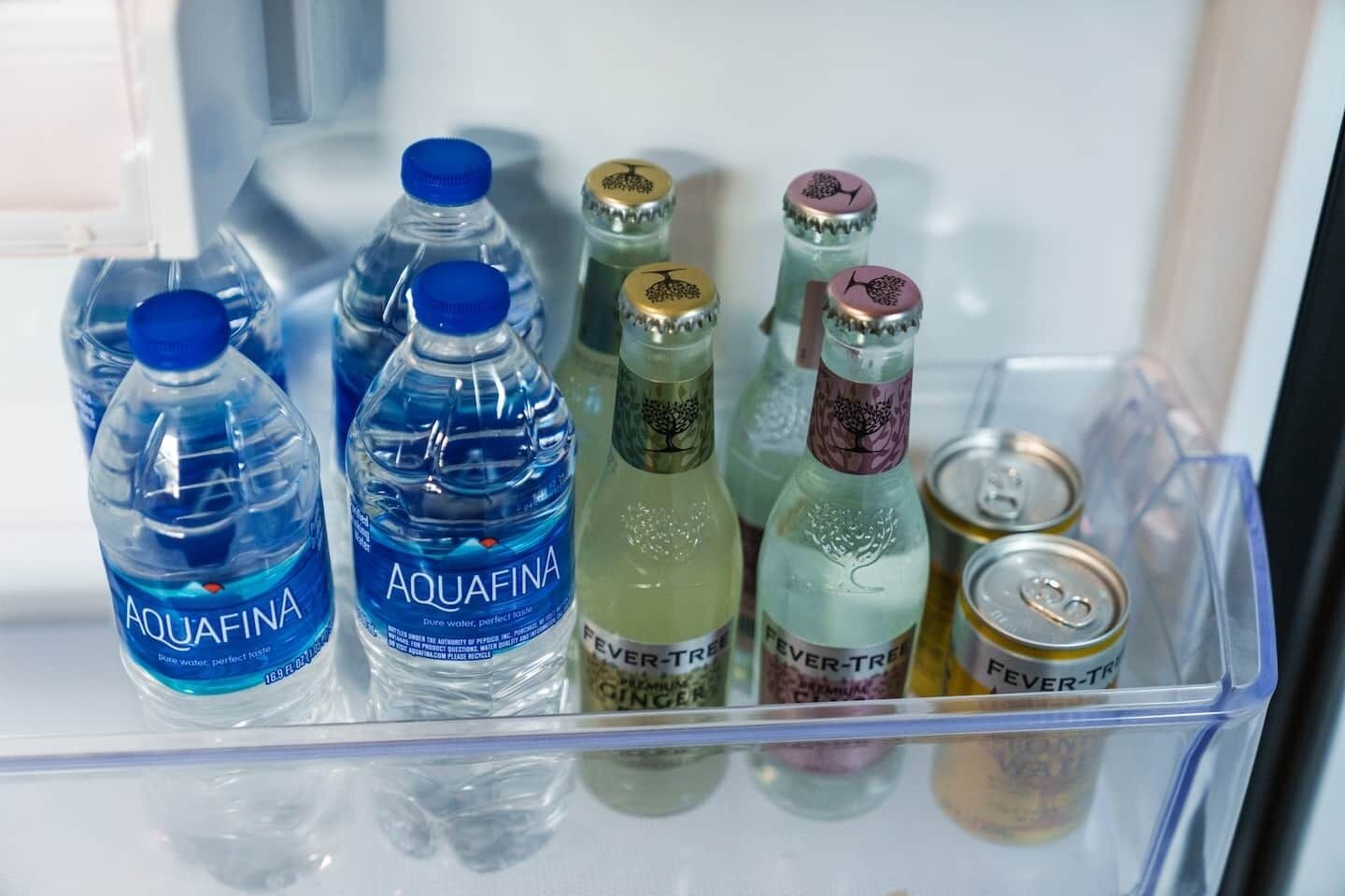Frigorifero con diverse bevande, tra cui bottiglie d'acqua Aquafina, bibite Fever-Tree e una lattina di Ginger Fever-Tree.